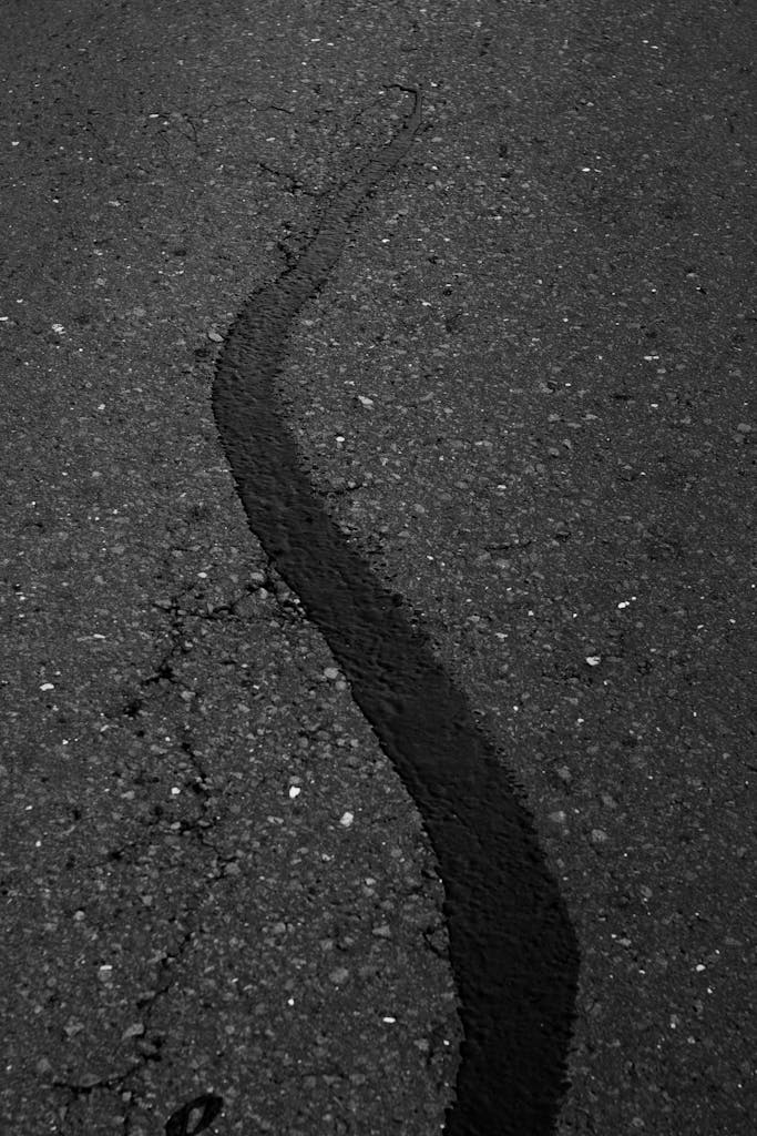 Detailed view of a road surface with a dark patch on cracked asphalt. Perfect for texture and construction themes.